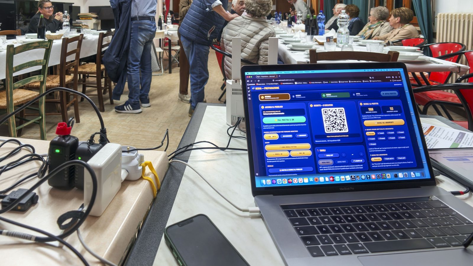 Regia di Quizzopoli con il QR code per entrare nel gioco dal telefono e il pubblico seduto a tavola