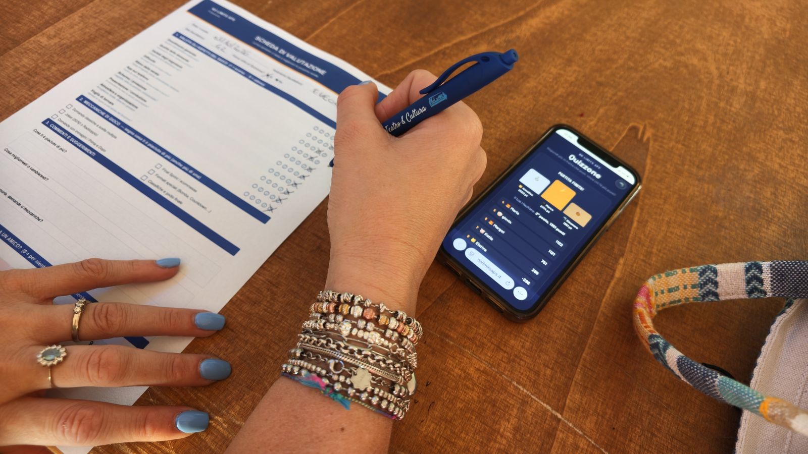 Telefono con l'app di Quizzopoli e scheda di valutazione durante la serata di prova